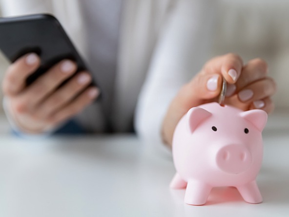 person putting money into piggy bank while using smartphone